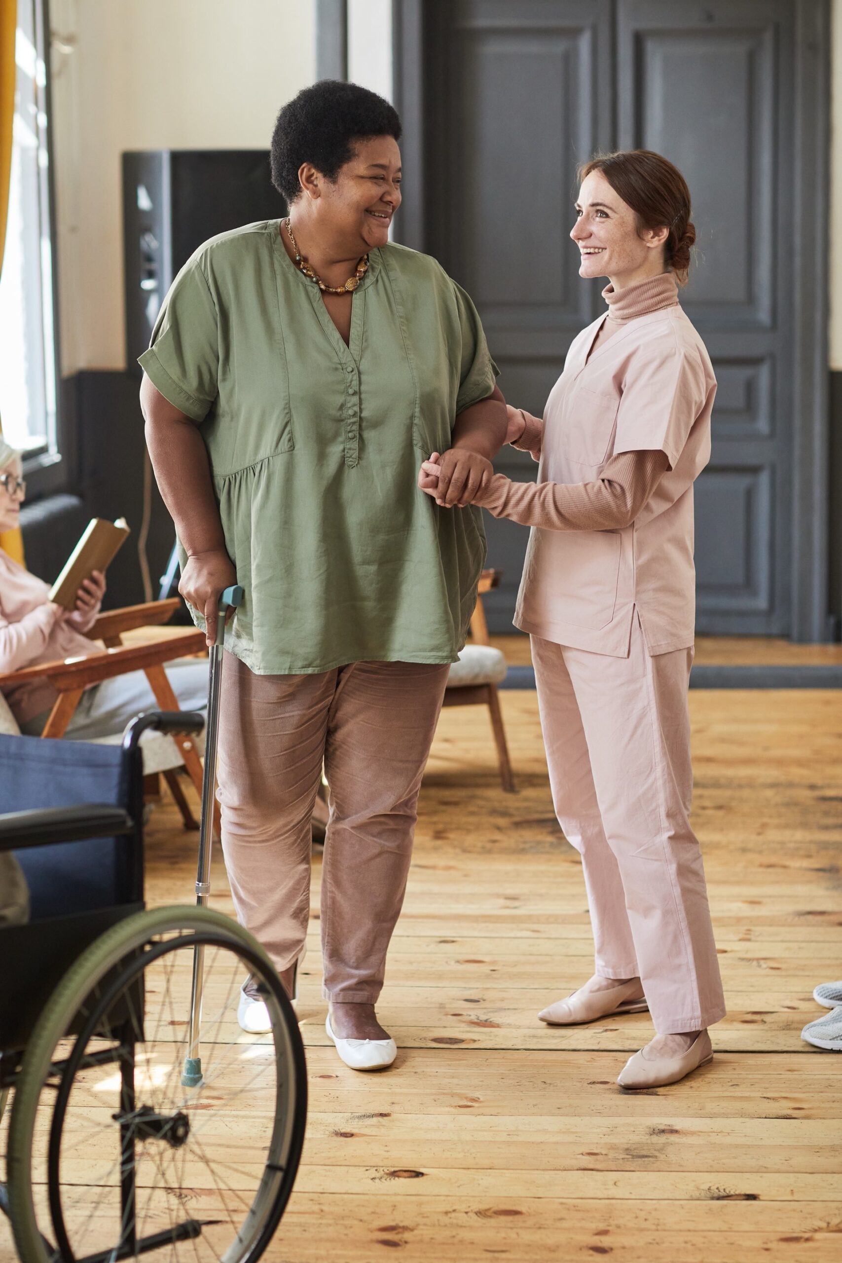 Vertical full length portrait of smiling young woman helping seniors in modern retirement home